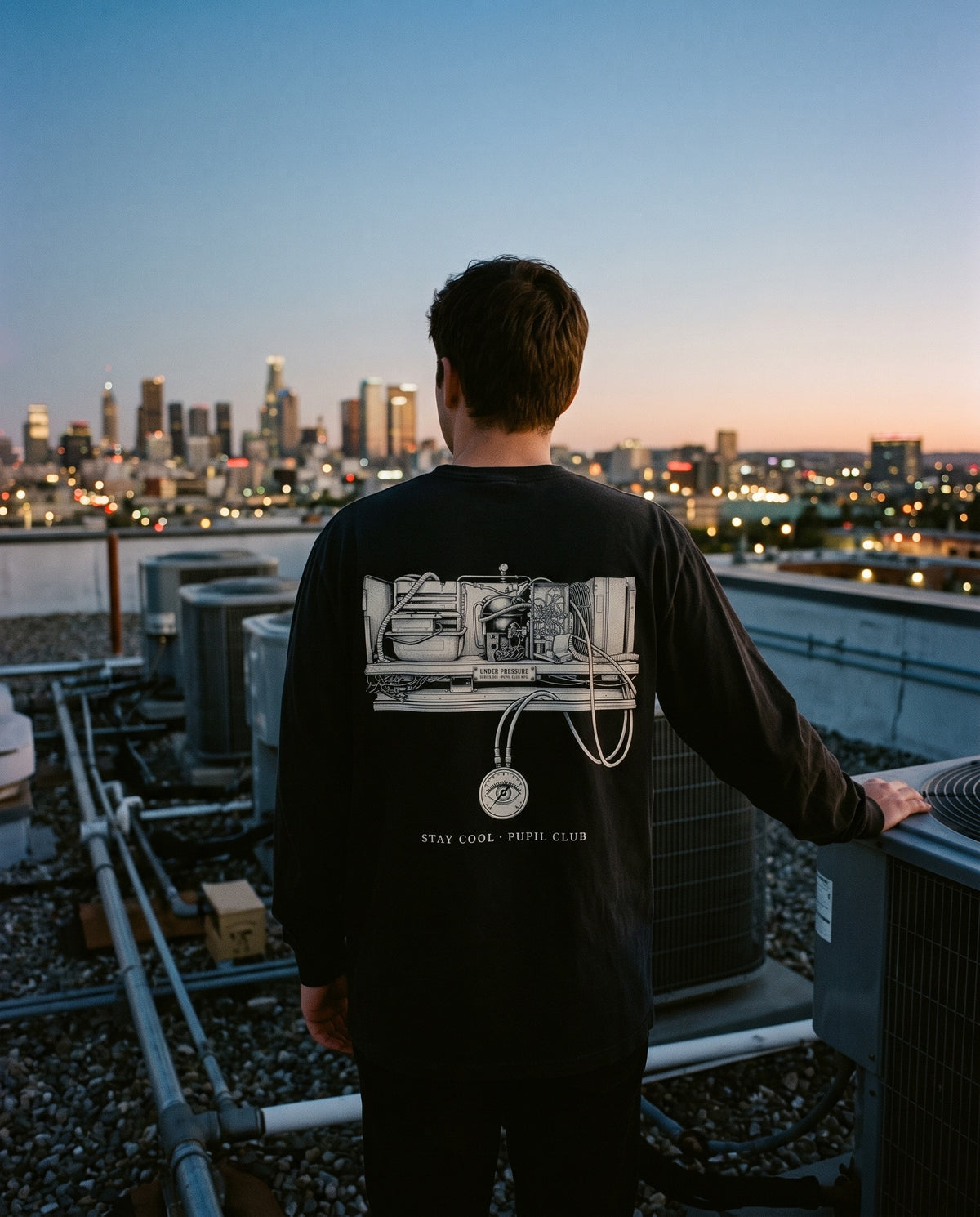 Under Pressure Long Sleeve back: engraved refrigeration unit with a hidden eye in the pressure gauge, worn on a rooftop at dusk